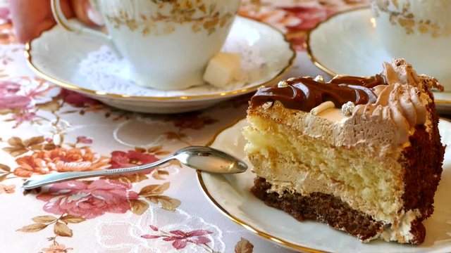 Coffee with milk and a slice of cake on a silver platter. Hot drink and dessert. Beautiful tablecloth on the table. Hand put the cup on the table.