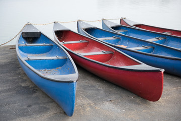 Red and blue rowing boats on the side of a boating pool on an overcast pale day. Exercise boating and rowing.
