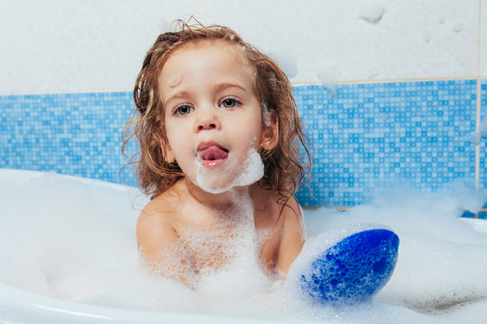 Little beautiful girl bathes in a bathroom, plays the fool and shows tongue. Fun bathing children. Positive hygiene. Independent child