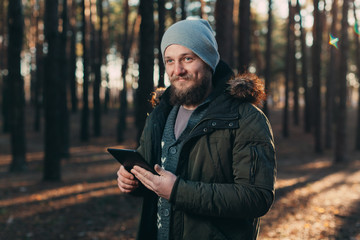 Portrait of adult man walking in the pine forest with digital tablet.