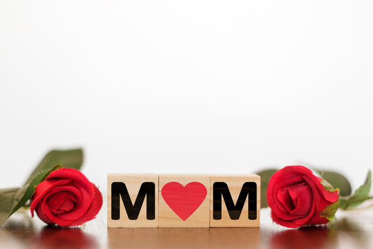 MOM word written on wooden cubes with red roses around. Mother's day concept