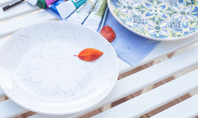 painted plates, plates on a white table, plates with paintings, plate with a sketch of the picture, on the plate is a red leaf