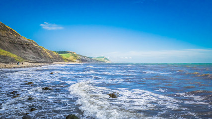 Waves on the sea / English Channel in Charmouth - English summer holidays place with English hilly countryside in the background. Golden Cap on jurassic coast in Dorset, UK. Photo with selective focus