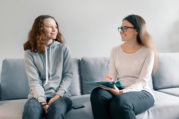 Young woman professional psychologist talking with teenager girl 14, 15 years old sitting in office...