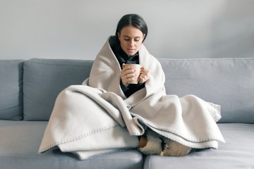 Naklejka premium Autumn winter portrait of young girl resting at home on the sofa with cup of hot drink, under warm blanket