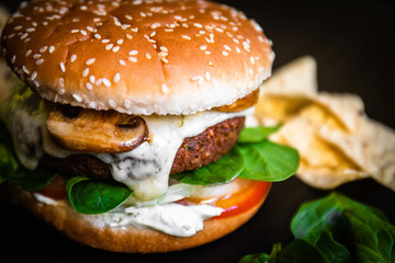 Hamburger vegetarian burger with falafel and vegetables salad tomato champignon and cheese tofu cheese all vegan food with nachos in blurred background