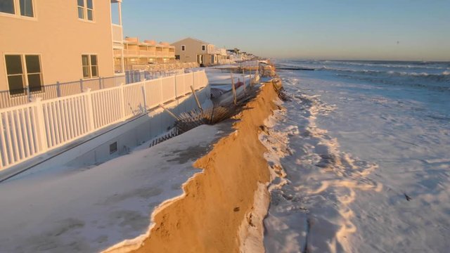 After a violent winter storm on the coast, high tide waves get dangerously close to severly damaged and eroded sand dunes protecting houses.