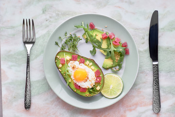 Baked Avocado boat with ham cubes, quail egg and cheese served with green rucola salad