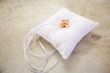 Closeup of a pair of wedding rings on a white pillow. Rings intertwined white ribbon. Pillow on white marble.