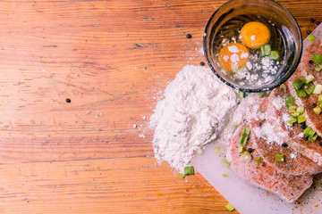 Raw Pork Loin chops on a cutting board with herbs, rosemary, thyme, chilli, salt, pepper on white cutting board. Broken eggs and flour for cooking batter. Copy space
