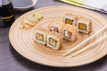 Sushi on a wooden plate with a glass of beer, soy sauce and natural wooden chopsticks on a light wooden table.