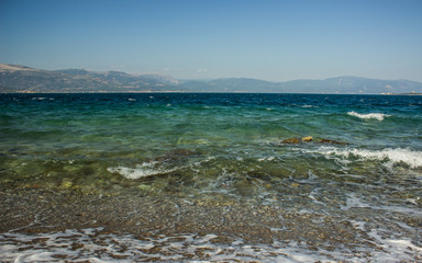 sea coast line tropic landscape with waves on vivid blue and green transparent water surface and mountain ridge silhouette background 