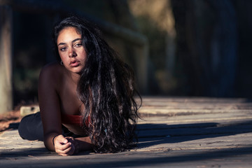 Mujer joven morena con el cabello suelto tumbada en el camino del bosque mirando a la cámara