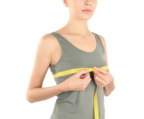 Young woman measuring breast size on white background, closeup. Cosmetic surgery