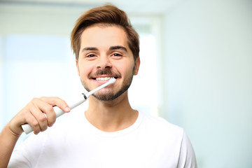 Portrait of young man with electric toothbrush on blurred background. Space for text