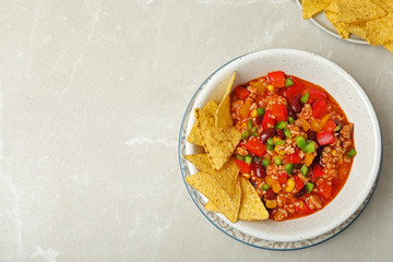 Chili con carne served with tortilla chips on grey table, top view. Space for text