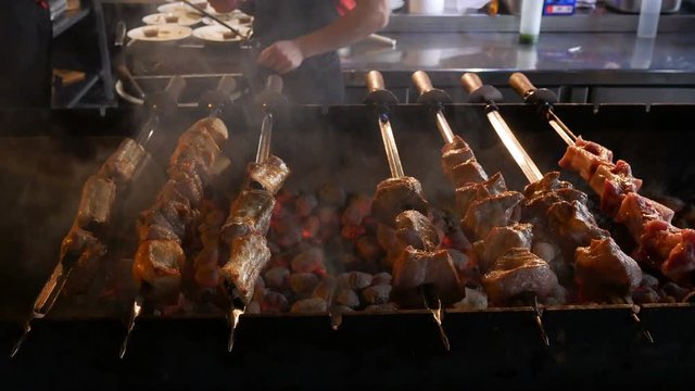 Cooking kebabs or barbecue in restaurant or cafe over charcoal. Preparing barbecue with delicious grilled meat on skewers is prepared on coals in kitchen of restaurant. Turn over meat on grill.