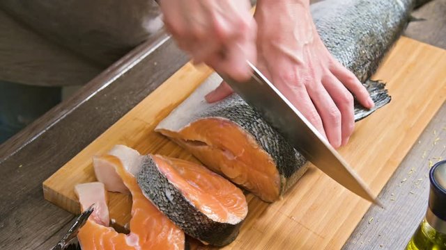 Close-up of female hands are cutting with a knife a large salmon on a wooden table of home cooking