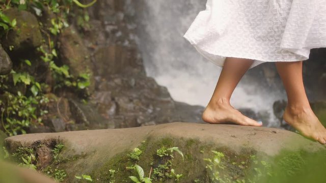 Female Walking Barefoot at Beautiful Natural Waterfall in Tropical Jungle. Calm and Carefree Lifestyle Travel 4K Slowmotion Footage. Bali, Indonesia.