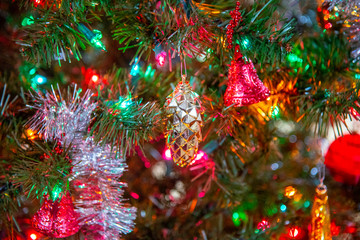 Obraz na płótnie Canvas A close-up or macro shot of a portion of a festively decorated and colorfully lit Christmas tree with bells, balls, tinsels and other hanging objects in a horizontal image format.