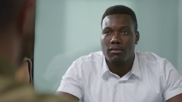 PAN shot of black businessman in casual white shirt discussing work with unrecognizable colleagues during meeting