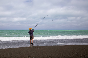 A man surf casting in the sea on a Canterbury beach in New Zealand