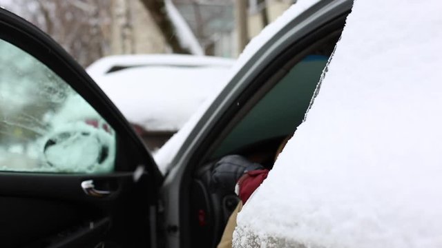 Man shake off snow from snowy legs before sit in car and drive away