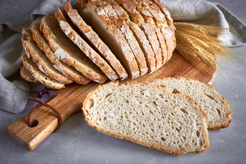 Slliced white round bread with wheat ears on wooden cutting board on gray stone