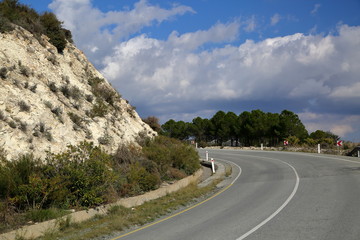 Road in the mountains, curve, sharp turn, arid hill on the left side, trees on the right, cloudy sky