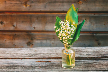 Bouquet of flowers beautiful smell blossom twigs lily of the valley or may lily in glass vase on rustic old wooden background. Garden in spring or summer. Blooming ecology nature concept