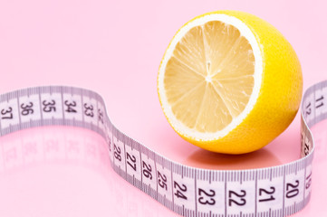 Sliced lemon and measuring tape on pink background. Diet concept.