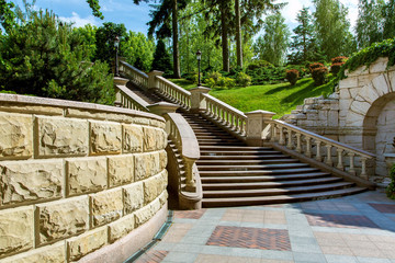 stone wall near the marble staircase with balustrades and iron lanterns against a landscape with green plants in the park garden of the mansion.