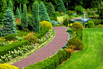 red pavement walkway in the backyard with landscape design and various bush plants and trees, top view of the walkway for a walk in the garden.
