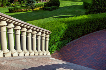 A staircase with stone steps and balustrade railings descends down the walkway along the hedge in the landscaped garden.