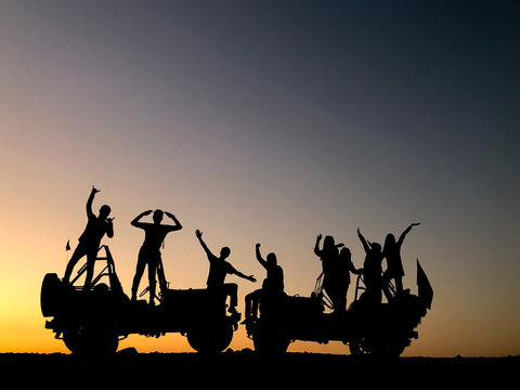 The silhouette of a group of people best friend having fun sitting and posing on a jeep over sunset background. friendship concept.