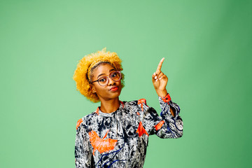 Young woman pointing up, isolated on green studio background.