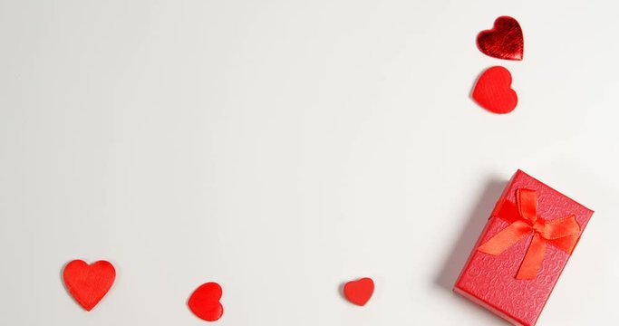 Red gift box and red hearts on white surface
