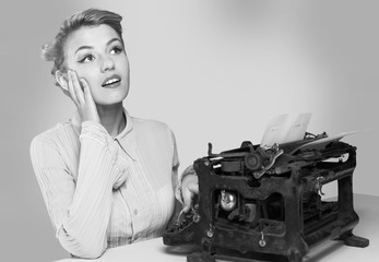 Fototapeta premium Young blonde female writer using typing machine, black and white