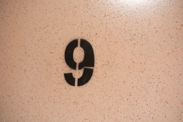 A close up on black stenciled number nine on orange wall