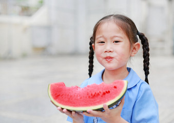 Adorable little Asian child girl in school uniform enjoy eating watermelon.