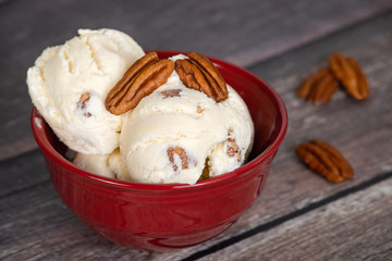 Delicious butter pecan ice cream served in a red bowl. Vintage wooden table background.