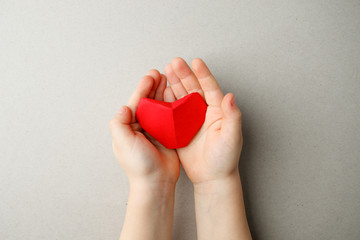 adult and childs hands holding red origami paper heart in hands on gray background copy space, flat lay. Valentines day, Mothers Day Love and health care Family insurance, Top view. World health day