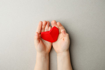 adult and childs hands holding red origami paper heart in hands on gray background copy space, flat...