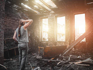 Man house owner stands inside his burnt house interior with burned furniture in arson and holding...