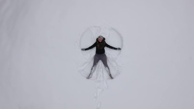 Blonde woman makes snow angel in winter snow.