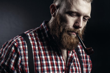 Handsome man or lumberjack, bearded hipster, with beard and mustache in red checkered shirt with smoking pipe