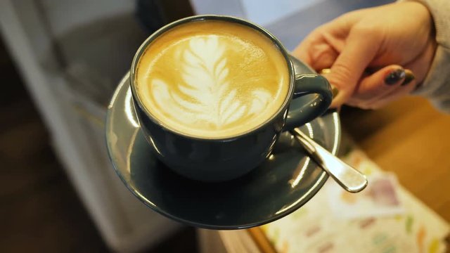 The waiter holds a cup of latte or cappuccino in his hand for serving to the client, the span of the chamber on top of the half-round