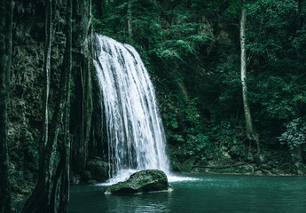 view of a beautiful waterfall in Thailand in a green jungle and clean environment in a moody green tone look surrounded with big trees and clear fresh green water which suggests an eco environment