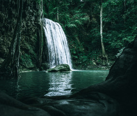 view of a beautiful waterfall in Thailand in a green jungle and clean environment in a moody green tone look surrounded with big trees and clear fresh green water which suggests an eco environment