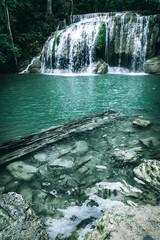 view of a beautiful waterfall in Thailand in a green jungle and clean environment in a moody green tone look surrounded with big trees and clear fresh green water which suggests an eco environment